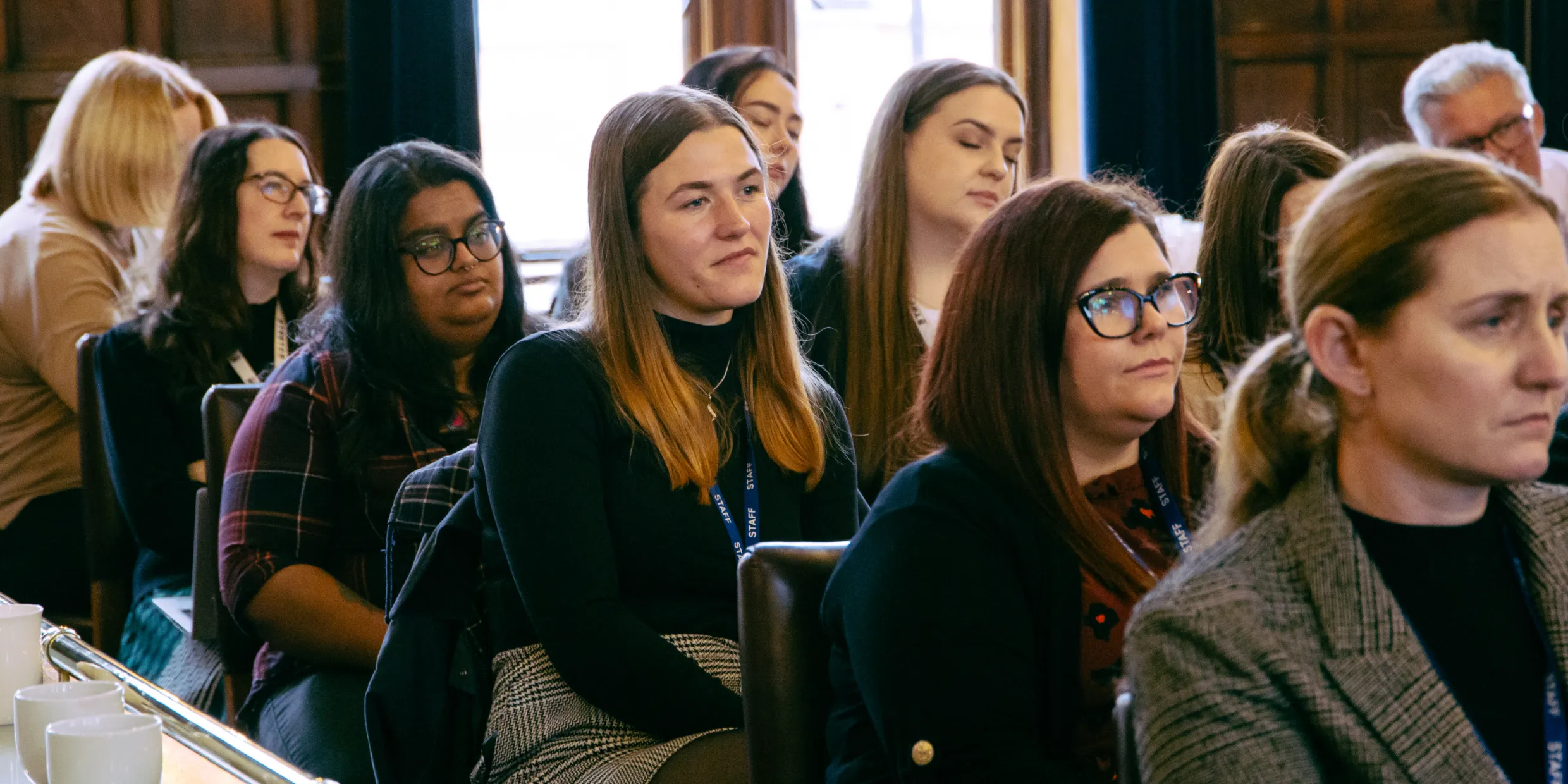 Attendees listening during a talk, seated in rows in a wood-panelled room.